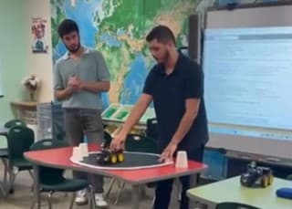Mentors demonstrating a wheeled robot on a classroom table while students watch